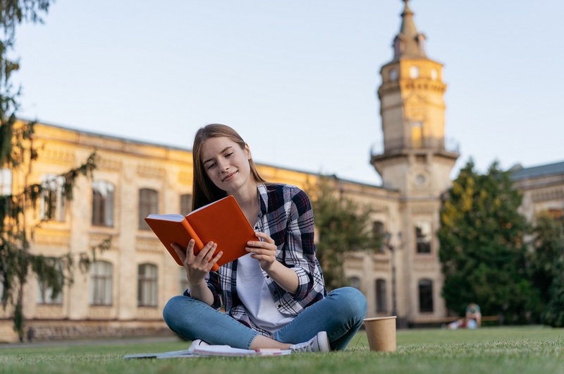 Medium university student studying reading book learning language exam preparation sitting grass education concept